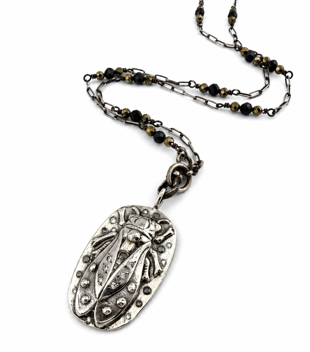 
                  
                    An antique-style silver pendant necklace featuring a detailed cicada insect charm, suspended from a chain with dark beads and antiqued metal links, set against a plain white background.
                  
                